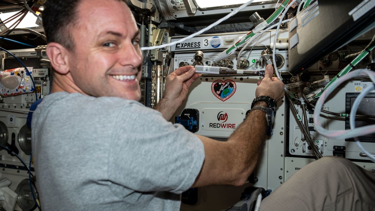 an astronaut floating in spies smiles while handling laboratory equipment