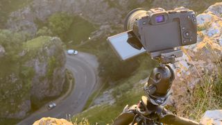 A Canon camera with a wide angle lens attached mounted to a Manfrotto tripod pointing down at the road in Cheddar Gorge from the top of a cliff