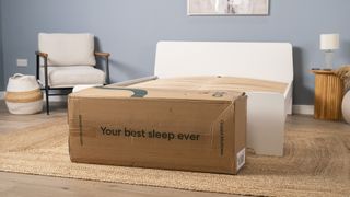 The Siena Memory Foam Mattress in a box on the floor in front of a bed frame, ready to be unboxed