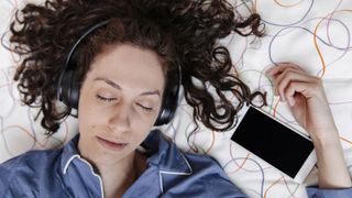 A woman with dark brown curly hair listens to a guided sleep meditation in bed