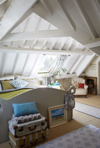 a master bedroom in converted loft with a sloping white ceiling, blue and yellow bedding, and a small armchair in the corner