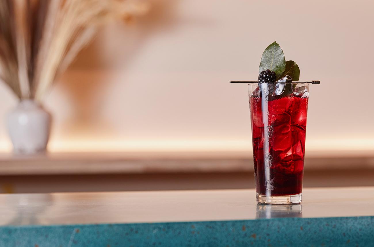 A red cocktail in a highball glass on a bartop