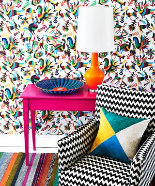 A colorful living room picture with patterned wallpaper and pink console table.