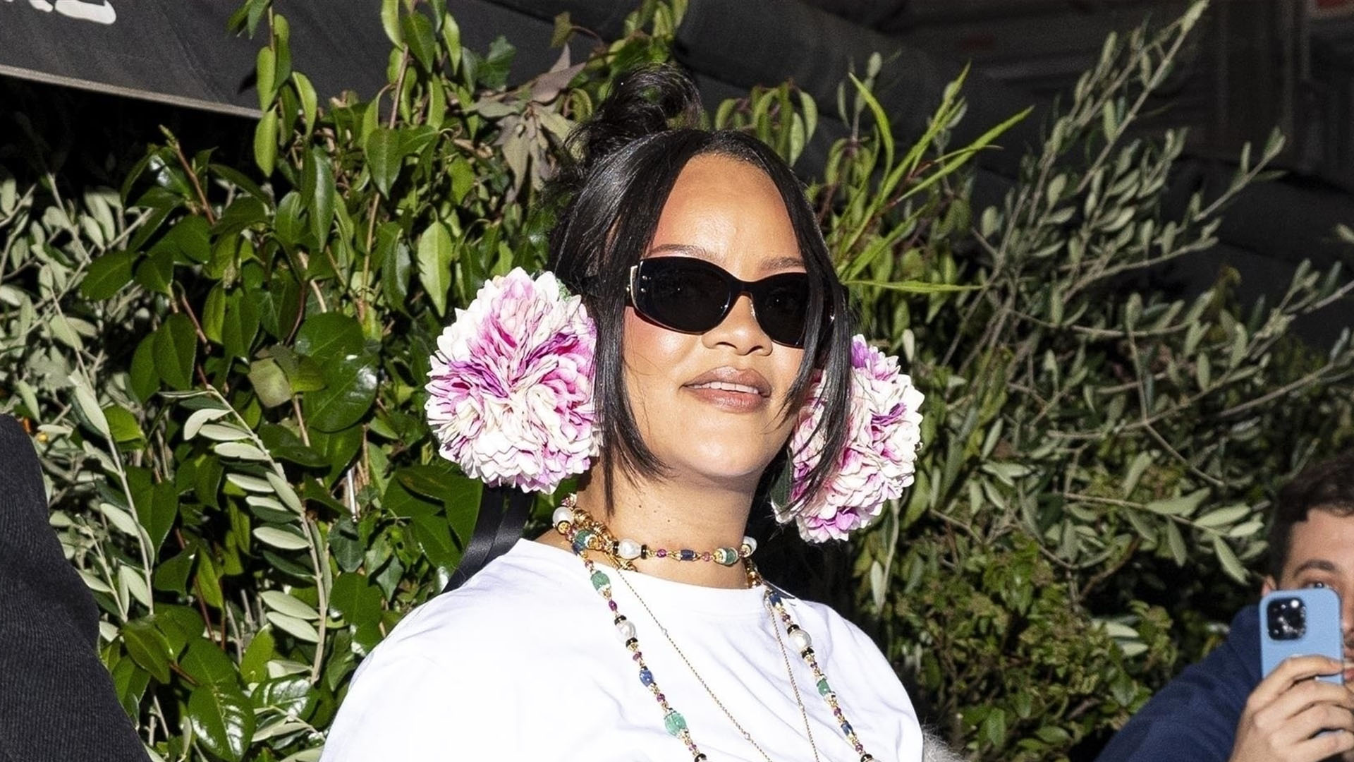 Rihanna wearing pink earmuffs, a white t-shirt, blue jeans, a white scarf, and pink satin heels
