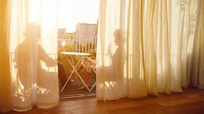 Couple enjoying balcony, silhouetted behind curtains in sunshine - for article on balcony privacy mistakes