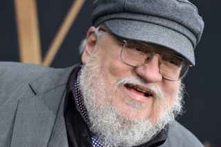 Fantasy and science-fiction author George RR Martin. He is wearing a grey suit and cap and is smiling.