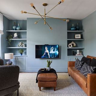 dusky blue living room with leather sofa with cushions tv and chandelier