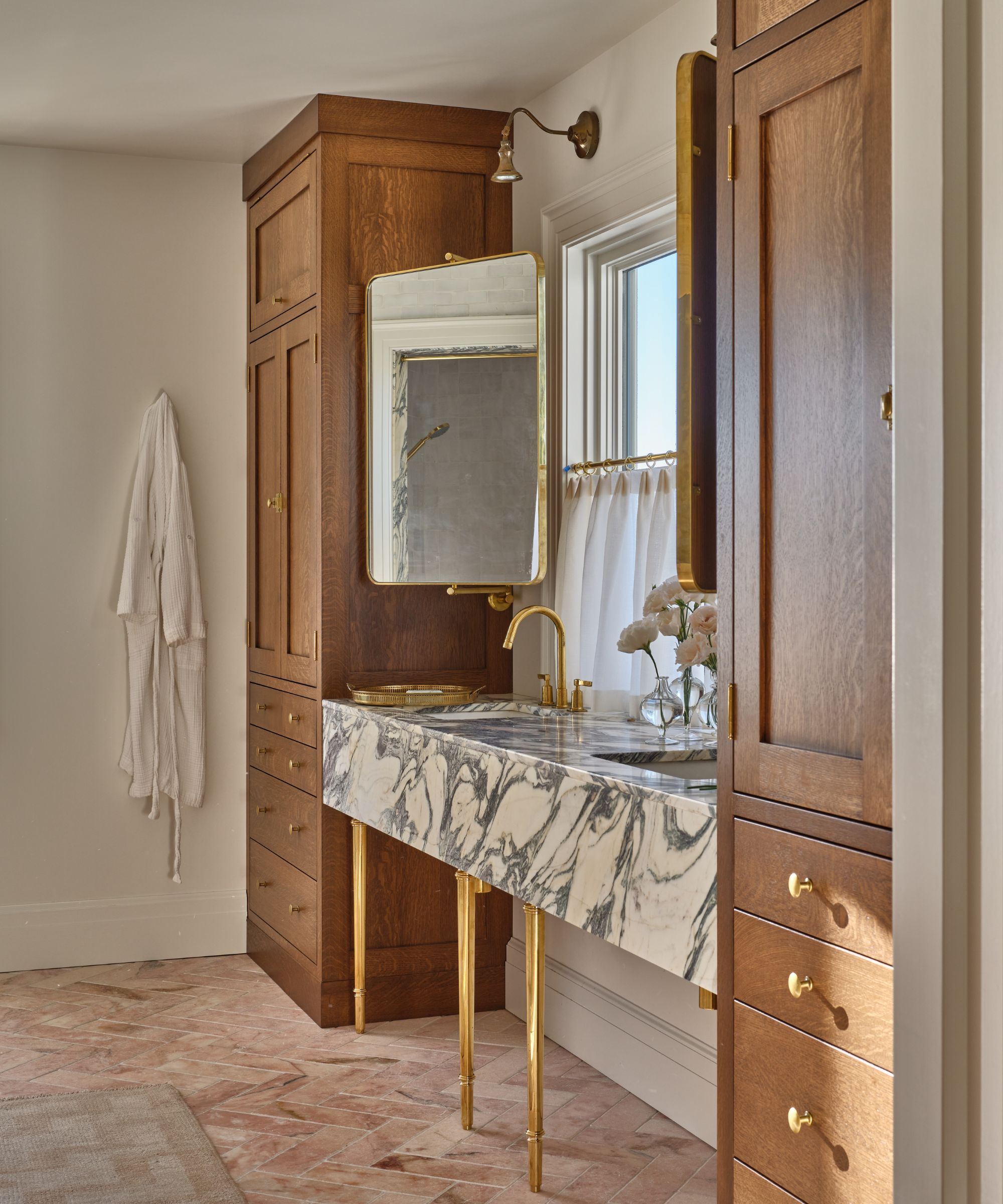 A luxury bathroom featuring a dramatic black-and-white veined marble vanity supported by brass legs, flanked by tall oak storage cabinets