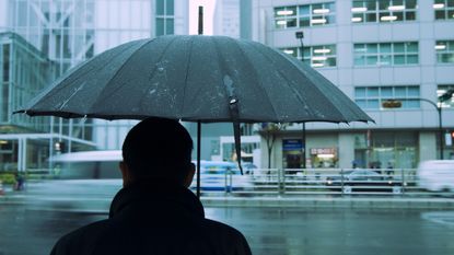 A man holds an umbrella while standing in the rain in front of a downtown building.