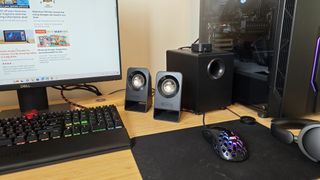 Black Logitech Z213 speakers sitting on a wooden desk