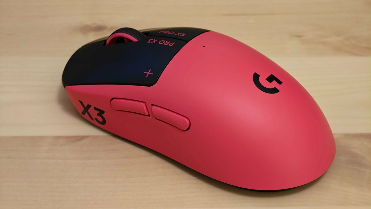 The Logitech G pro X3 Superstrike gaming mouse in pink placed on a light-coloured wooden desk.