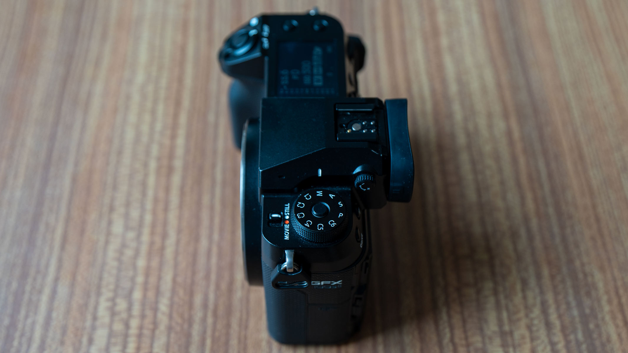 The top of the Fujifilm GFX 100S II, showing controls, on a wooden table.