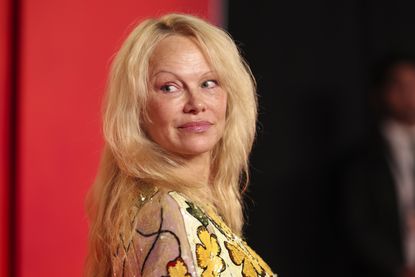 A headshot of Pamela Anderson on a red carpet looking over her shoulder