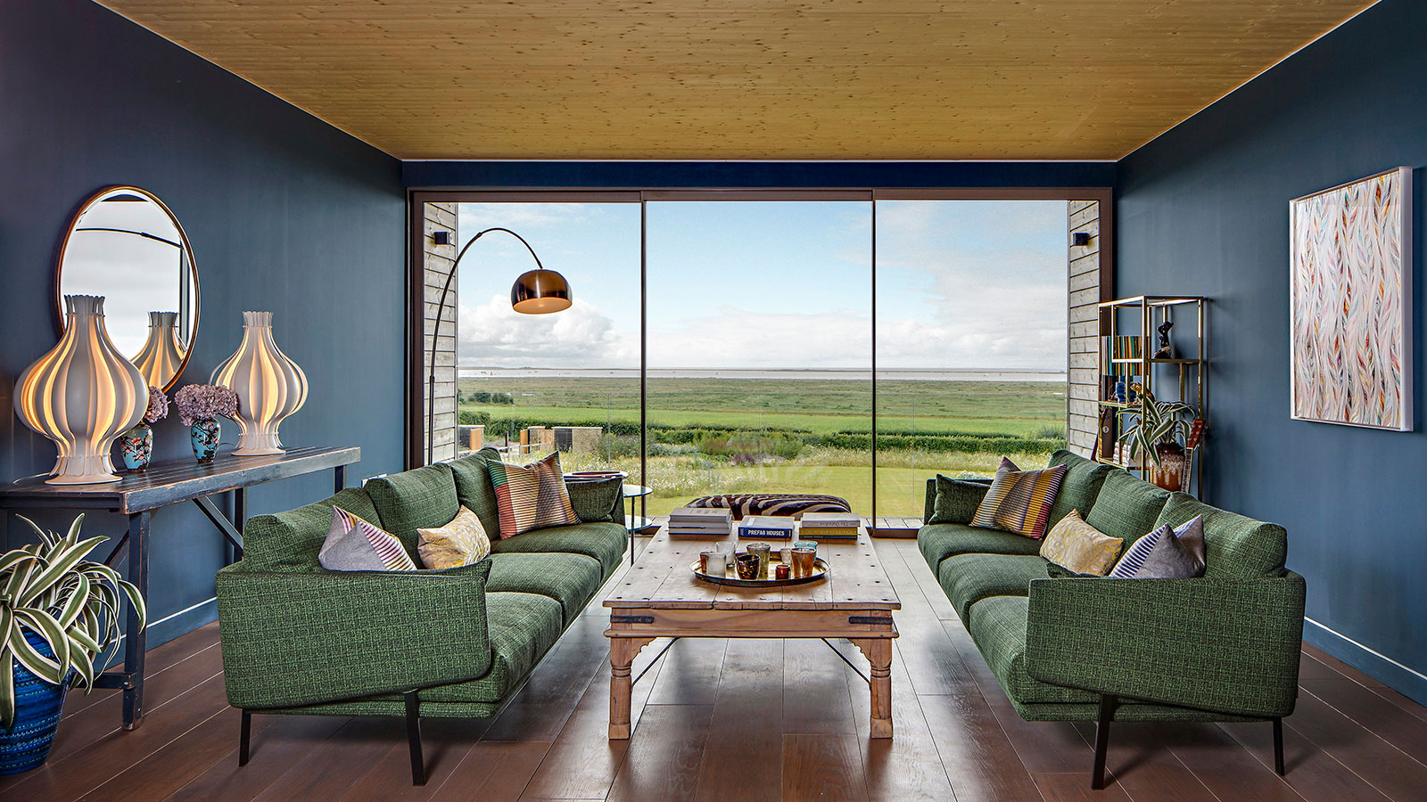 modern living space with two green sofas and dark blue painted walls and a fully glazed end wall with contemporary sliding doors overlooking a rural view