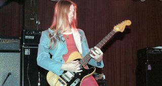 A young Steve Morse wears a red T-shirt and matching pants, and a light-blue jacket as he plays his FrankTele live in 1983.