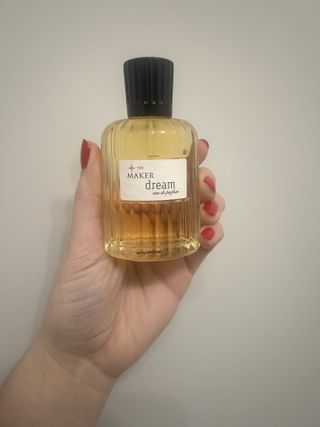 hand holding up bottle of the maker dream perfume against grey wall