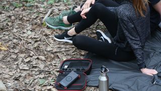 The OutXE W20 Waterproof Wireless Solar Power Bank in black and red is photographed in its open carry case in a forest setting