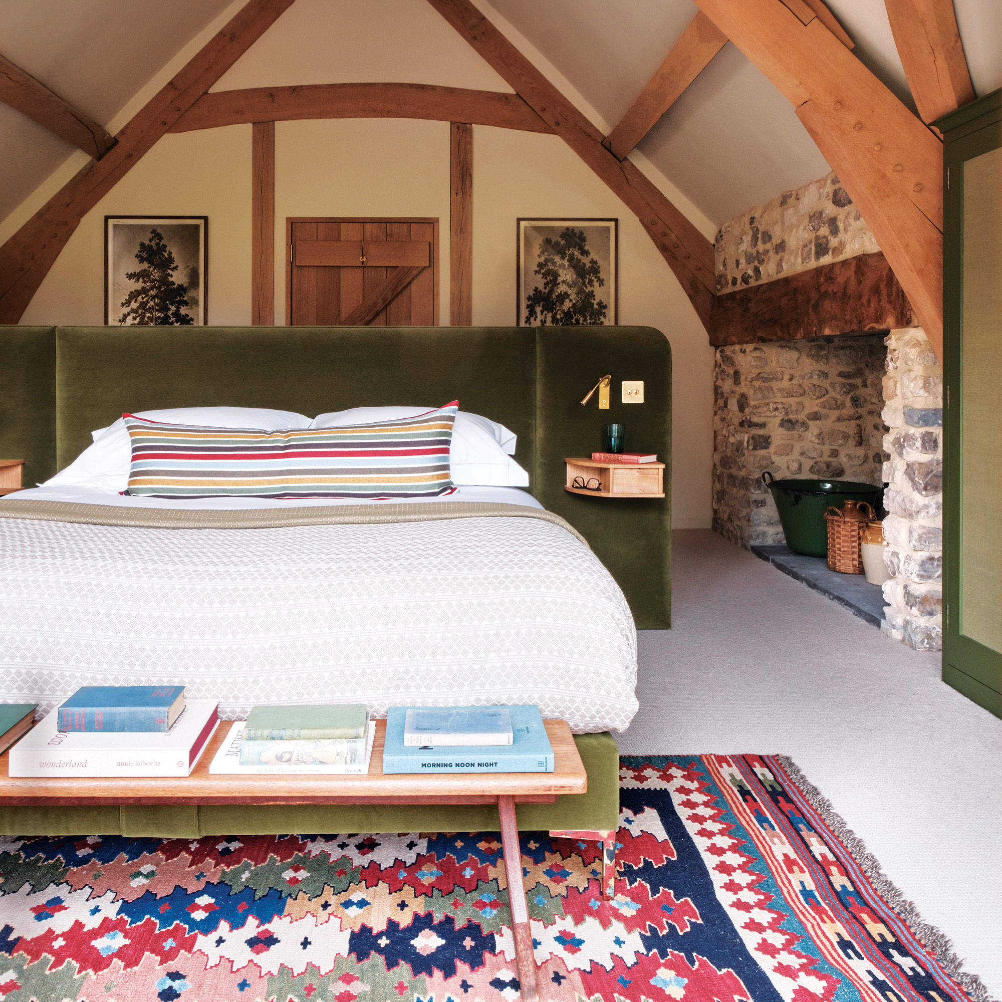 attic bedroom with beamed ceilings with the white bed in the middle of the room with oversized freestanding green velvet headboard