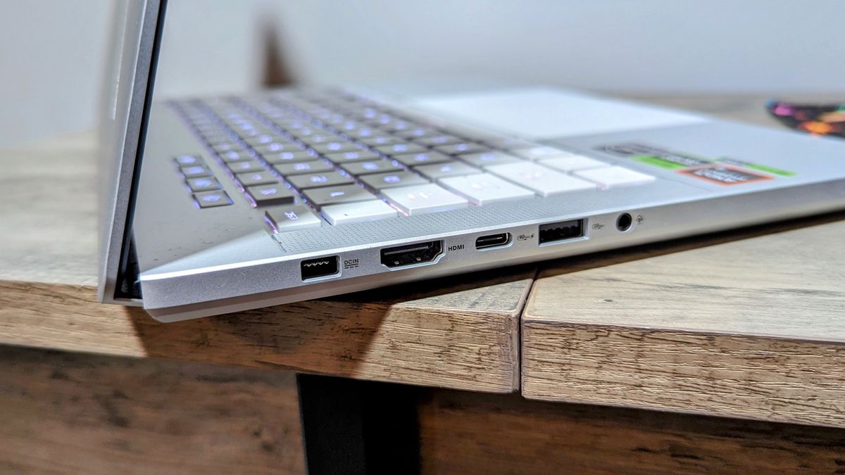 Asus Zephyrus G14 (2024) open on a brown table, highlighting ports on the left, including power, HDMI, a USB Type-C, a USB Type-A, and headphone jack.