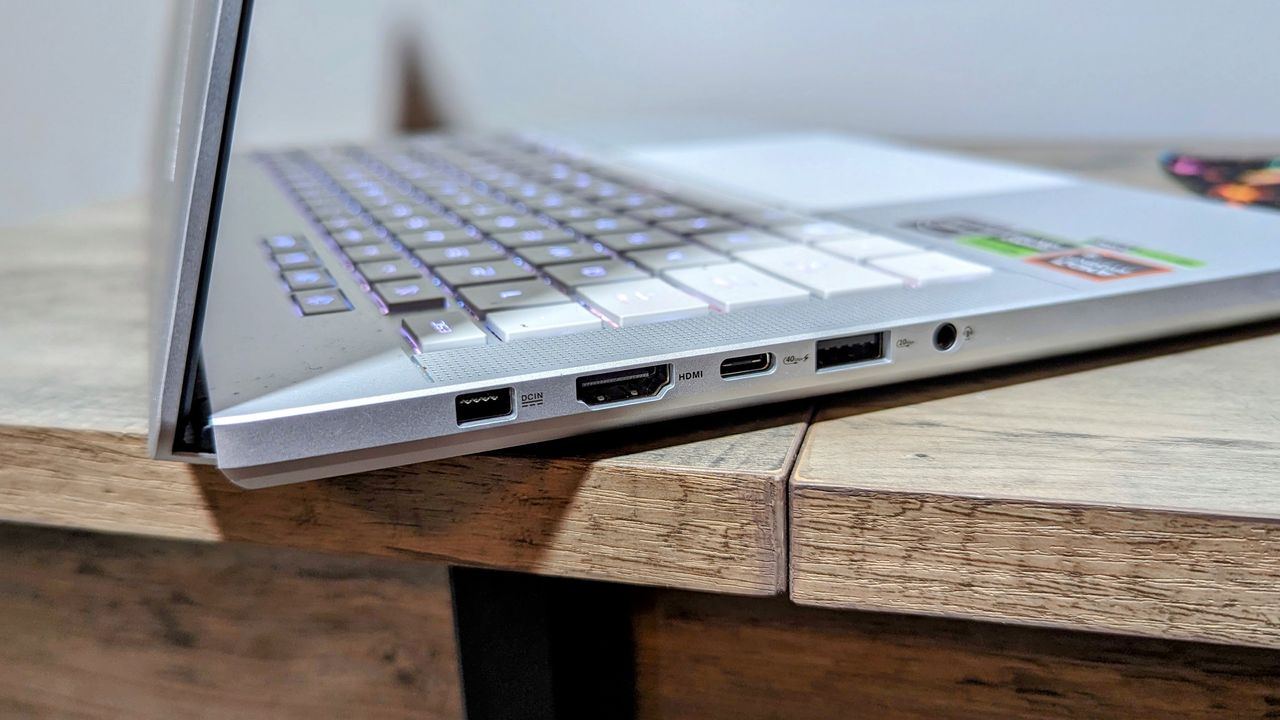 Asus Zephyrus G14 (2024) open on a brown table, highlighting ports on the left, including power, HDMI, a USB Type-C, a USB Type-A, and headphone jack.