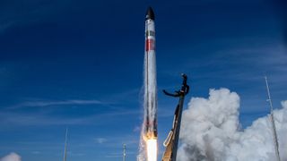 a white, red and green rocket launches into a blue sky.