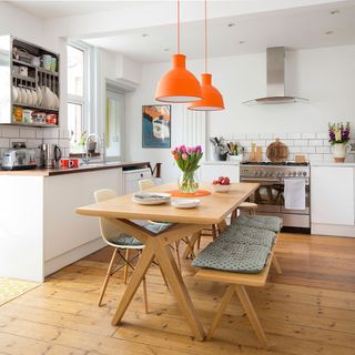 White kitchen with wooden floor, orange pendant lights and table and chairs