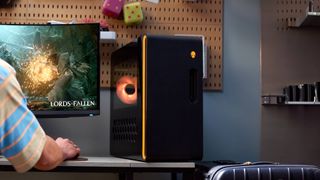 Alienware Aurora R16 on desk with orange LEDs and person on left playing Lords of the Fallen 