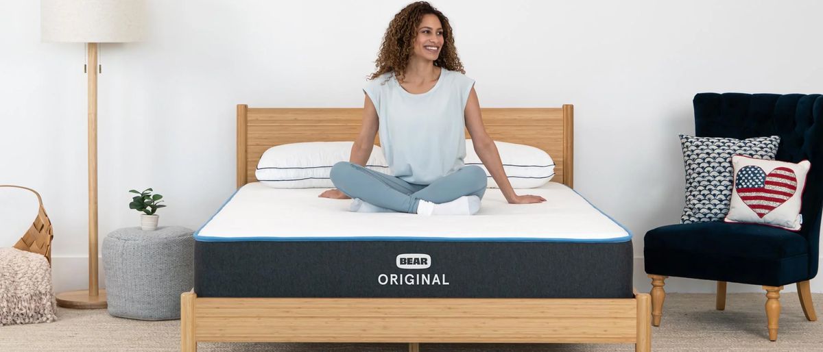 A Bear Original memory foam mattress on a bed frame in a bedroom with a woman sitting on top of the bed.