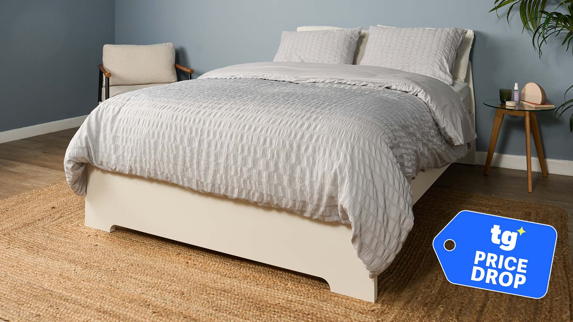 The Saatva Classic mattress in a bedroom, dressed in bed clothes, with a Tom's Guide price drop deals badge in the bottom right corner