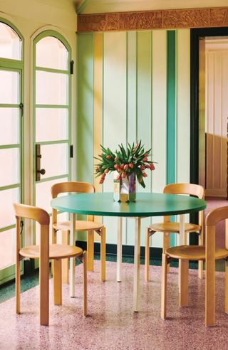 Colorful, modern dining room with green dining table, yellow dining chairs, textured green walls