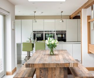 A compact dining area with rustic wood and benches in front of a sleek modern kitchen with built-in appliances and light green bar stools