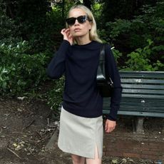 A woman wearing a navy sweater, tan skirt, sheer socks, and black tabi shoes