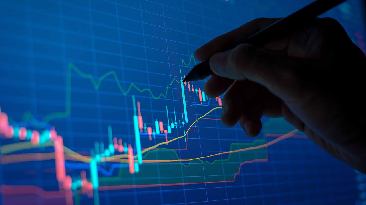 closeup of shadowed hand with pen and blue stock market chart