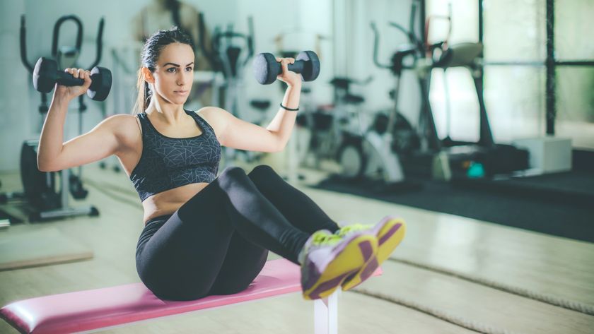 Woman performing a Z press with dumbbells in an overhead press position with legs extended