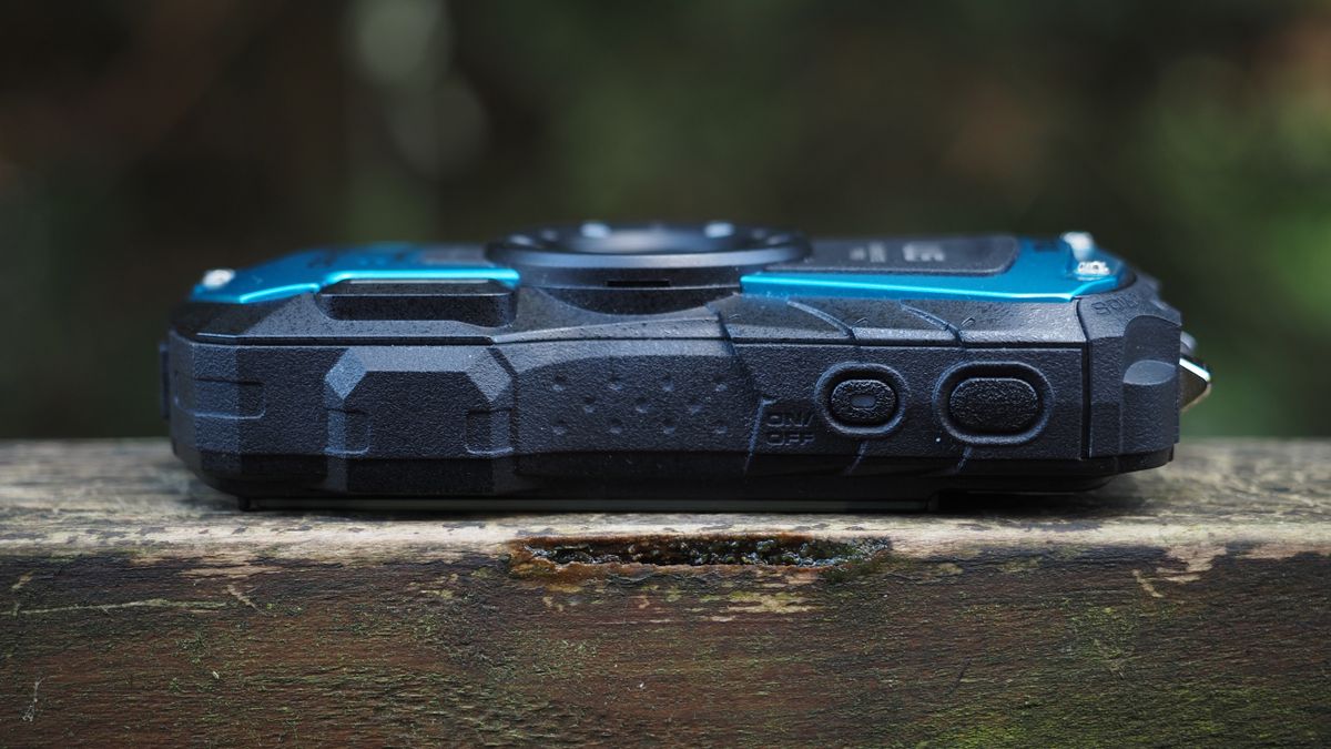 Close up of a Pentax WG-90 sitting on a wooden surface in front of woodland