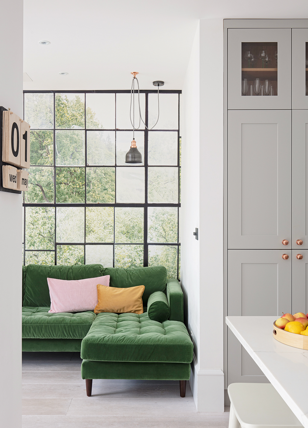 living area off a kitchen with a green velvet corner sofa and mirror grid wall covering