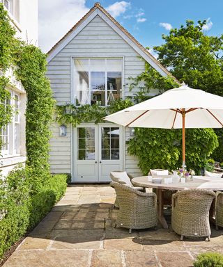Designing a patio in a small country garden with table, chairs and white parasol.