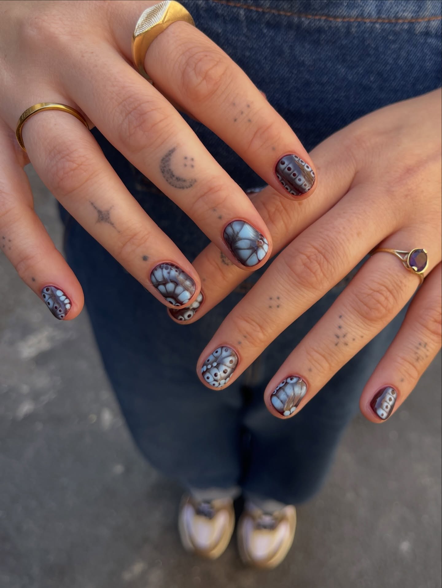 Short nails with detailed blue-gray butterfly wing designs outlined in dark polish