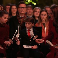 Princess Charlotte, Prince Louis and Kate Middleton holding lit candles and sitting at a carol service