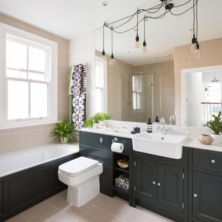 Modern country bathroom with dark grey painted built-in vanity unit with white countertop and string pendant lighting above a mirrored panel