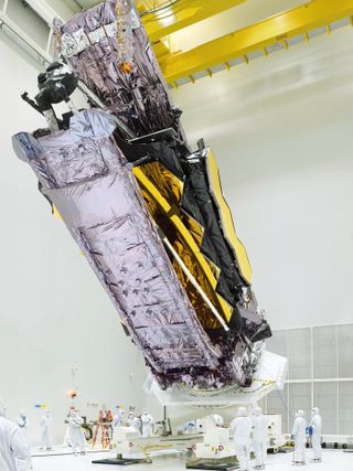 Webb towers over bunny suited technicians in its cleanroom at Europe's Spaceport.