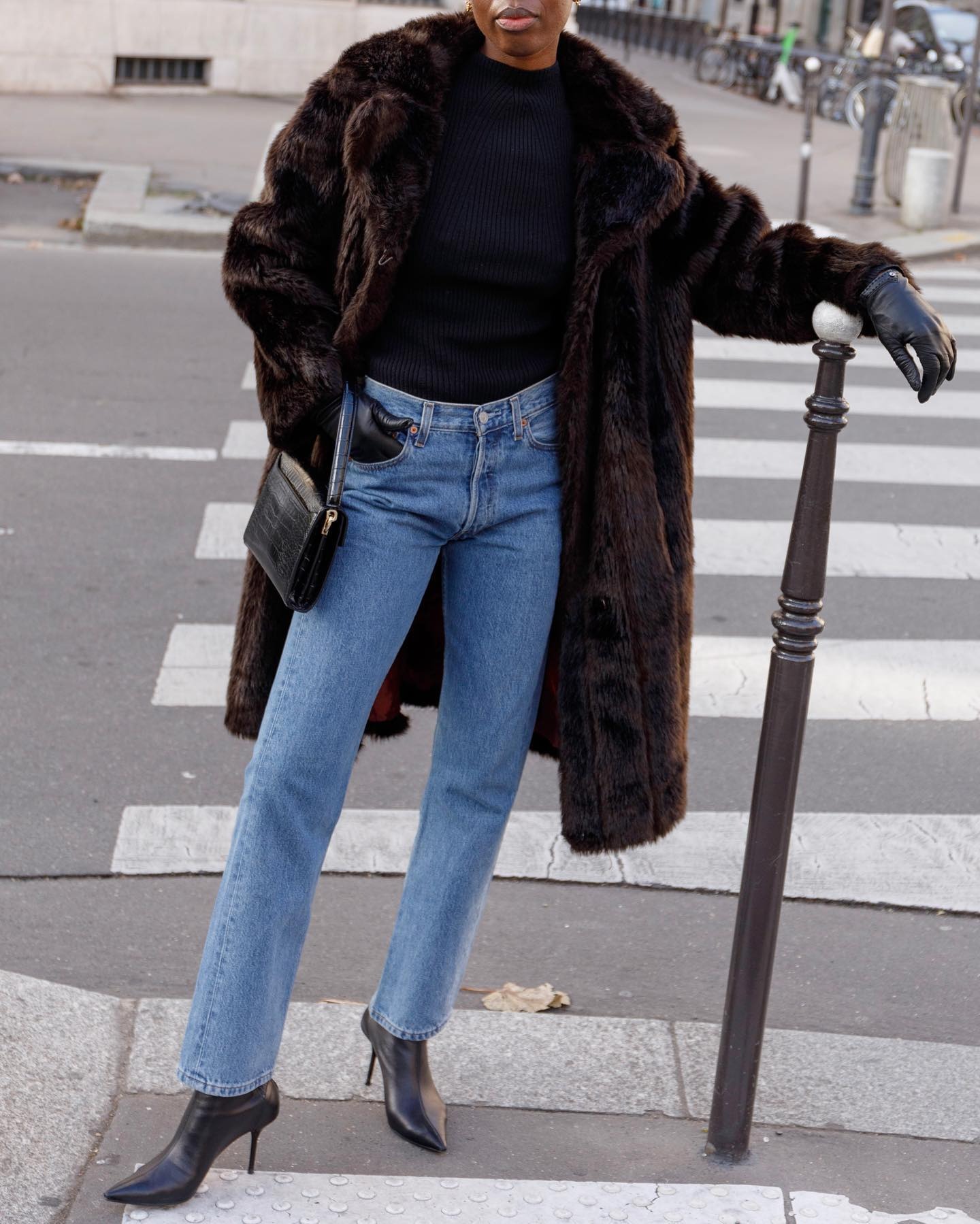 @sylviemus_ wearing a fur coat, black turtleneck sweater, light-wash jeans, and black ankle boots.