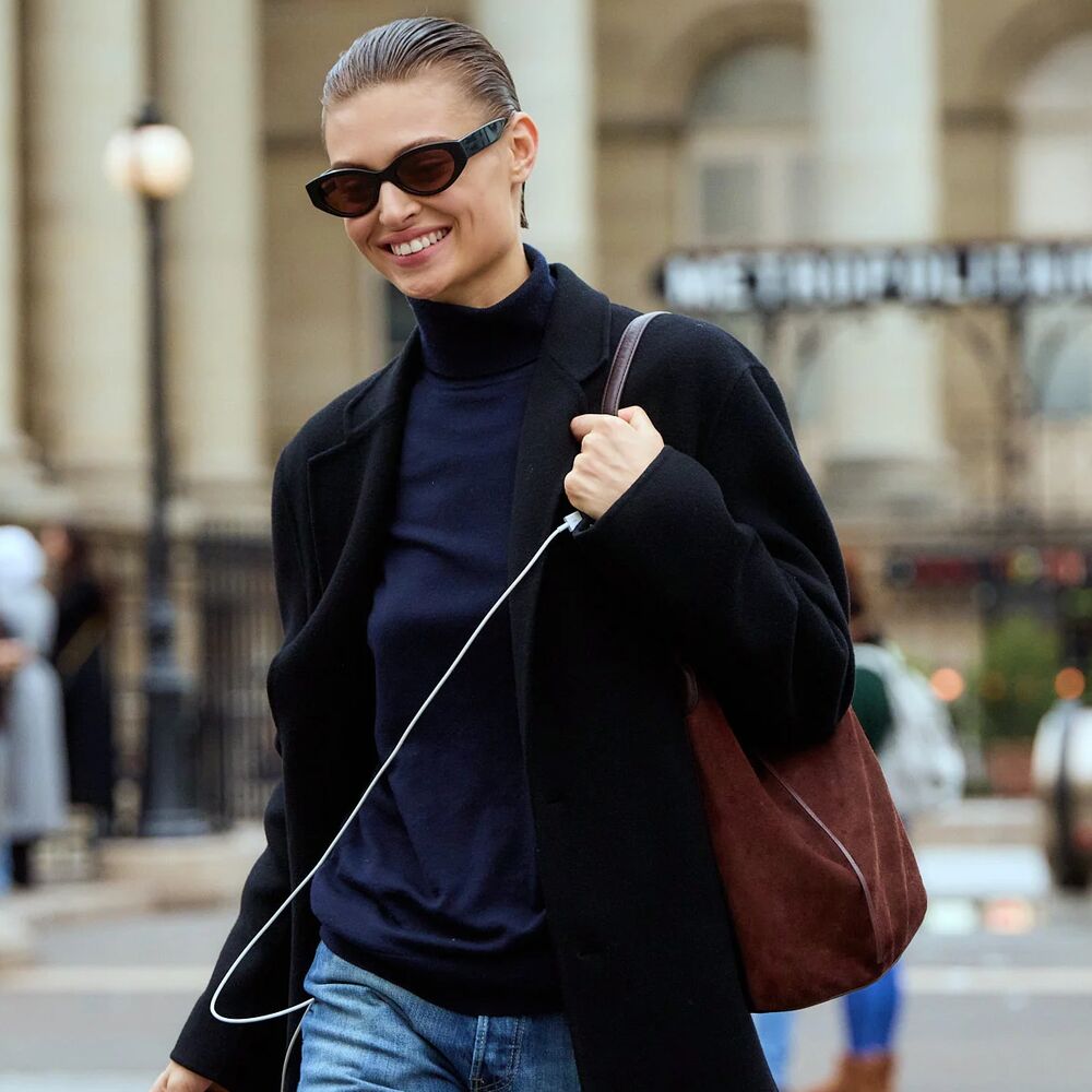Woman wearing blue turtleneck, black coat, brown suede bag, and jeans in Paris