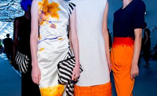 Models wear orange and white dresses and black top with orange skirt