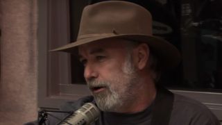 Tim Wilson in a cowboy hat speaking into a microphone in a studio on The Bob and Tom Show