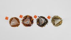 A row of four teabags with loose tea beneath them