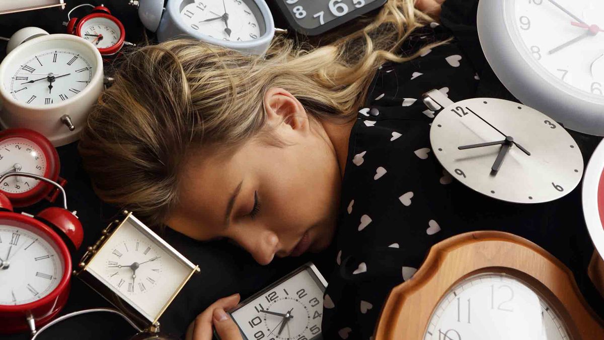 The best times to sleep and wake-up: A woman asleep surrounded by alarm clocks