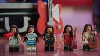 Lego Secret Storage set showing a red megaphone, blue vinyl disc, notebook and red guitar arranged on a Malibu-branded case, with a minifigure visible inside a small screen, against a blurred poster-covered backdrop.
