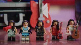 Lego Secret Storage set showing a red megaphone, blue vinyl disc, notebook and red guitar arranged on a Malibu-branded case, with a minifigure visible inside a small screen, against a blurred poster-covered backdrop.