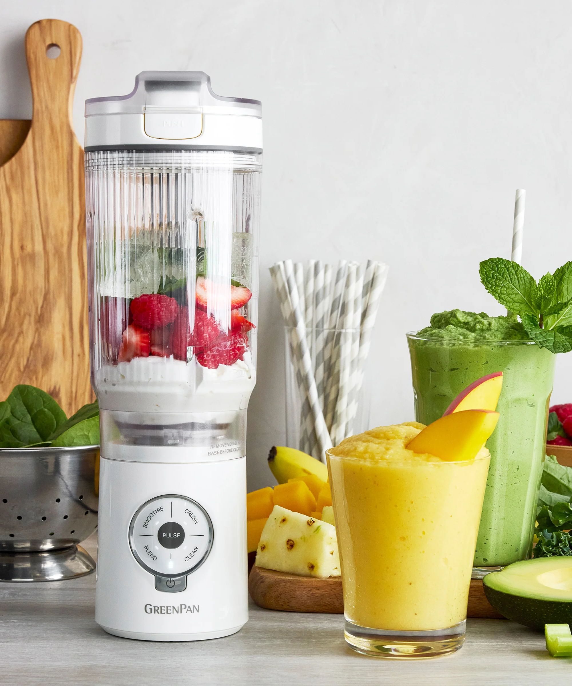 A white GreenPan spin &amp;amp; go blender with fresh fruit inside beside a glass of a yellow smoothie.